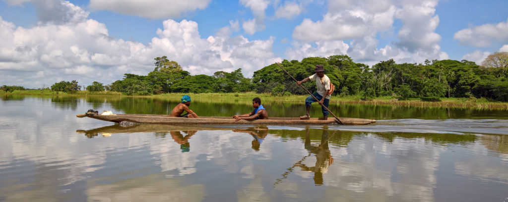 Photo of three Indigenous men in their traditional canoe travelling down the Sepik River in Papua New Guinea